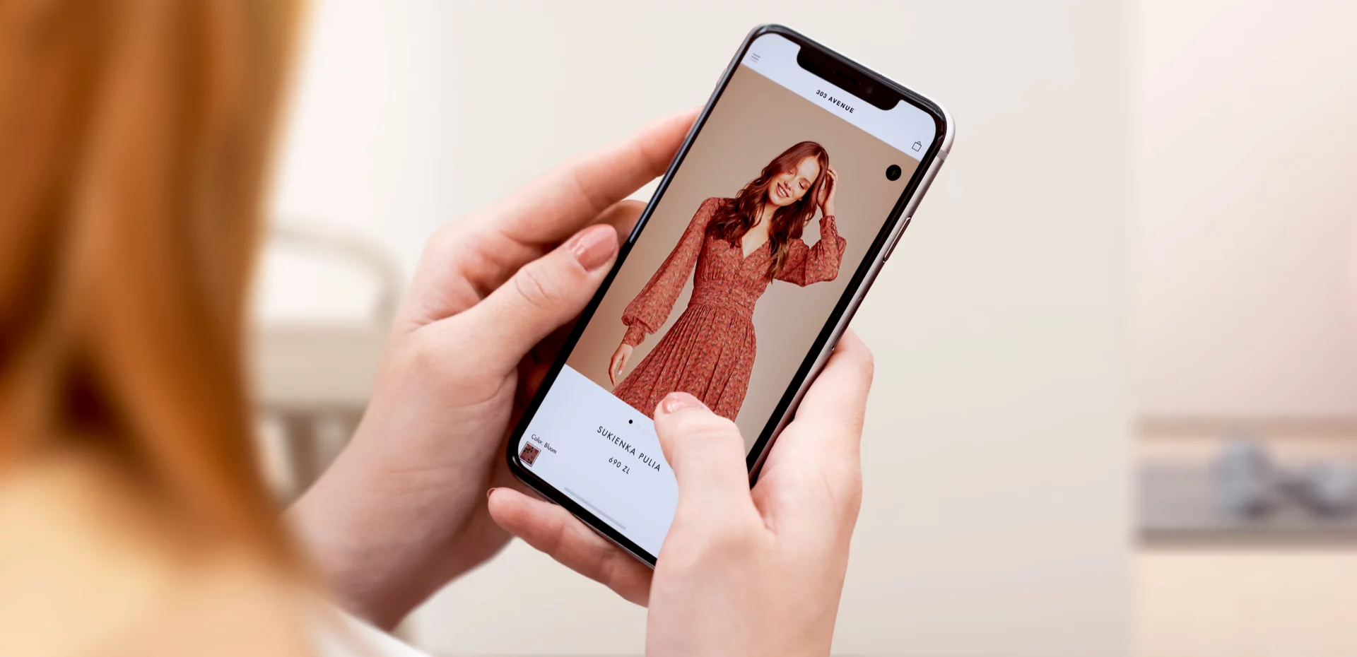 Person holding a smartphone displaying an online store page featuring a woman in a red floral dress.