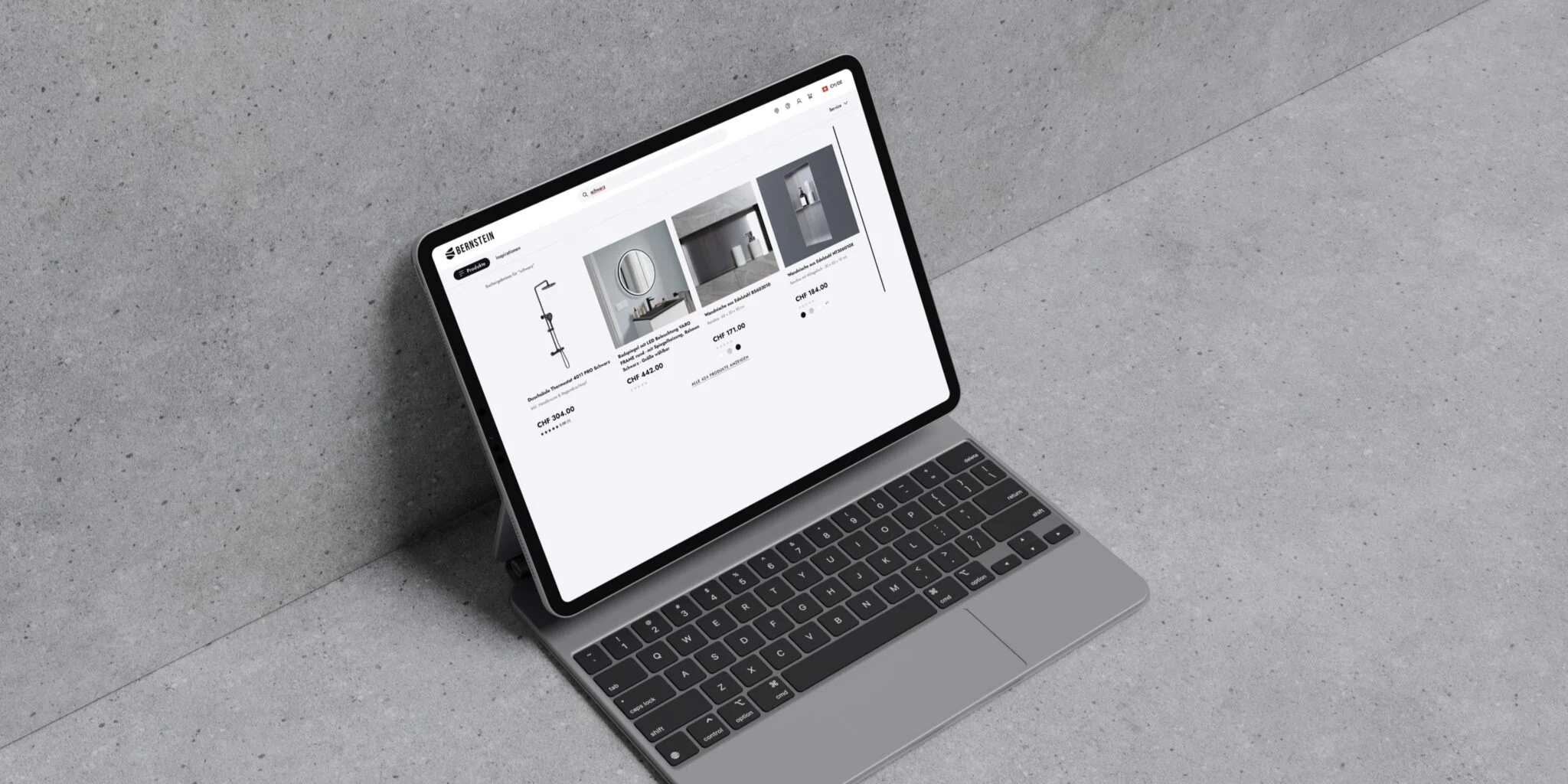 Tablet with keyboard displaying an online store page for Bernstein bathroom products against a gray concrete background.