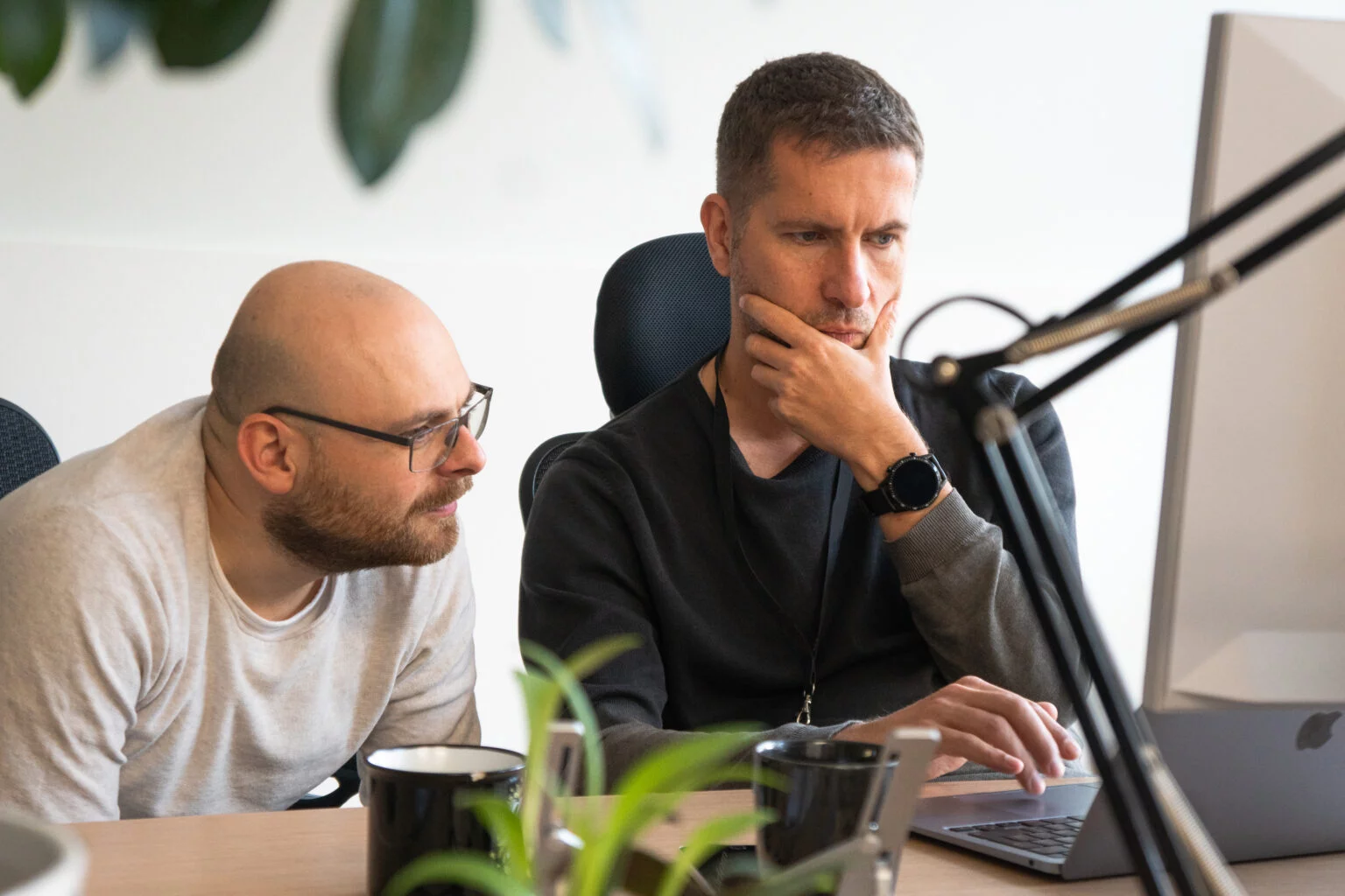 Two men focused on a laptop screen during a discussion in an office setting.