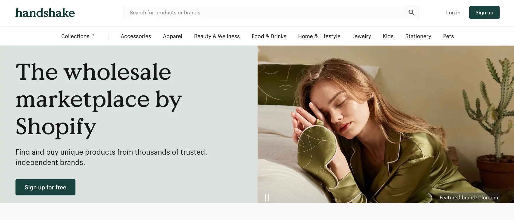 Woman in green satin pajamas resting her head on her hands next to a bed with abstract face pillow and a potted cactus plant in the background.