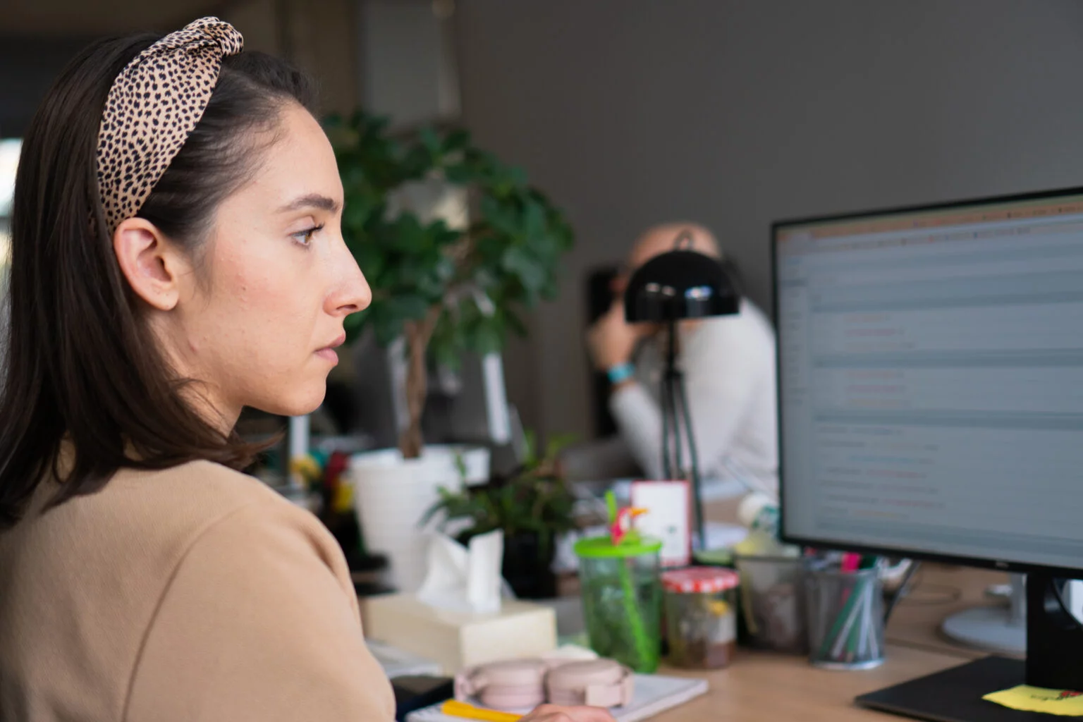 Woman with a leopard print headband focused on her computer screen in an office setting.