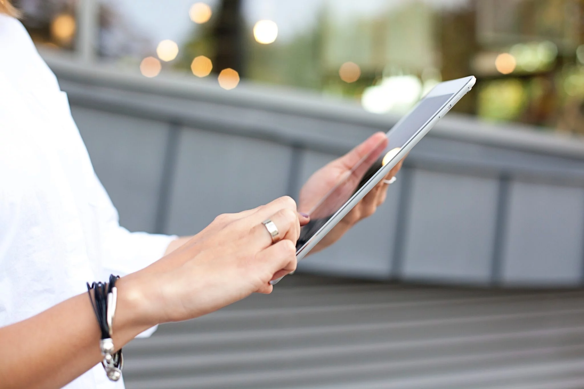 Close-up of a woman's hands tapping a tablet outdoors, illustrating mobile shopping on headless Shopify stores