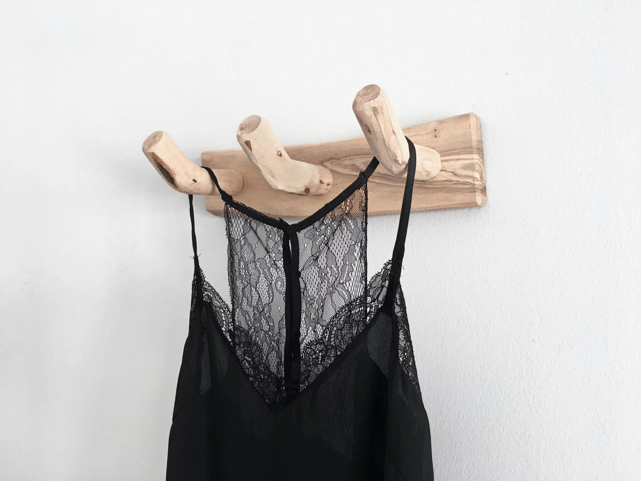 Black lace-trimmed slip hanging on a wooden wall hook against a white wall, representing a lingerie store