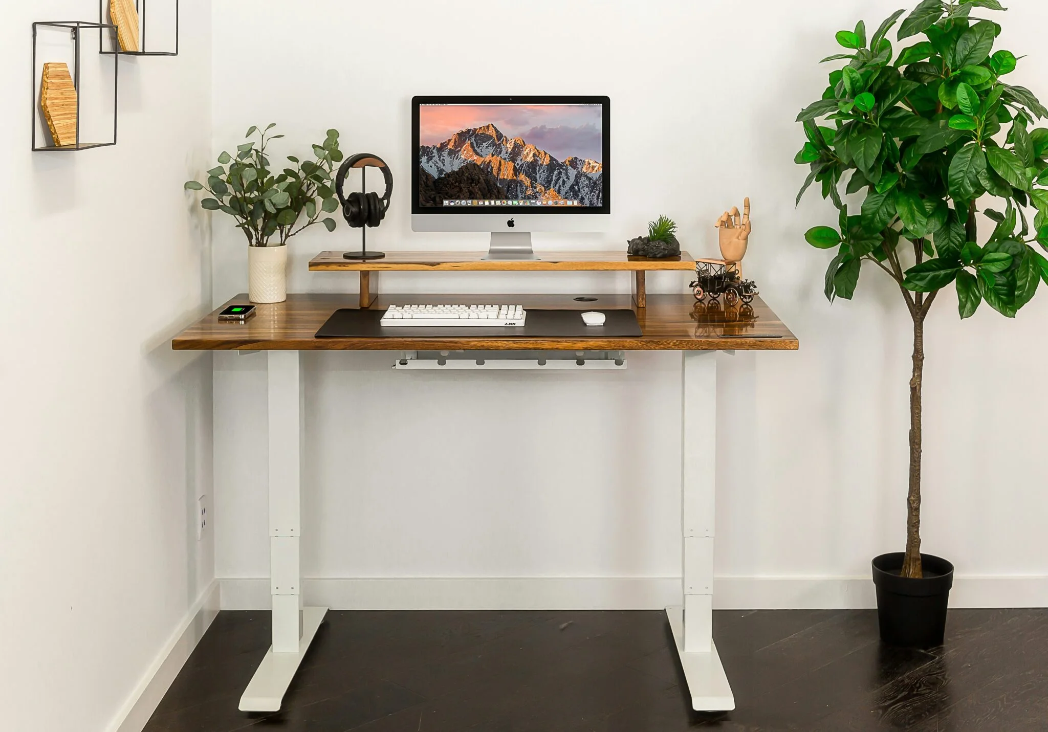 Height-adjustable desk with walnut top, iMac, headphones and plants in a bright room, an example of configurable furniture