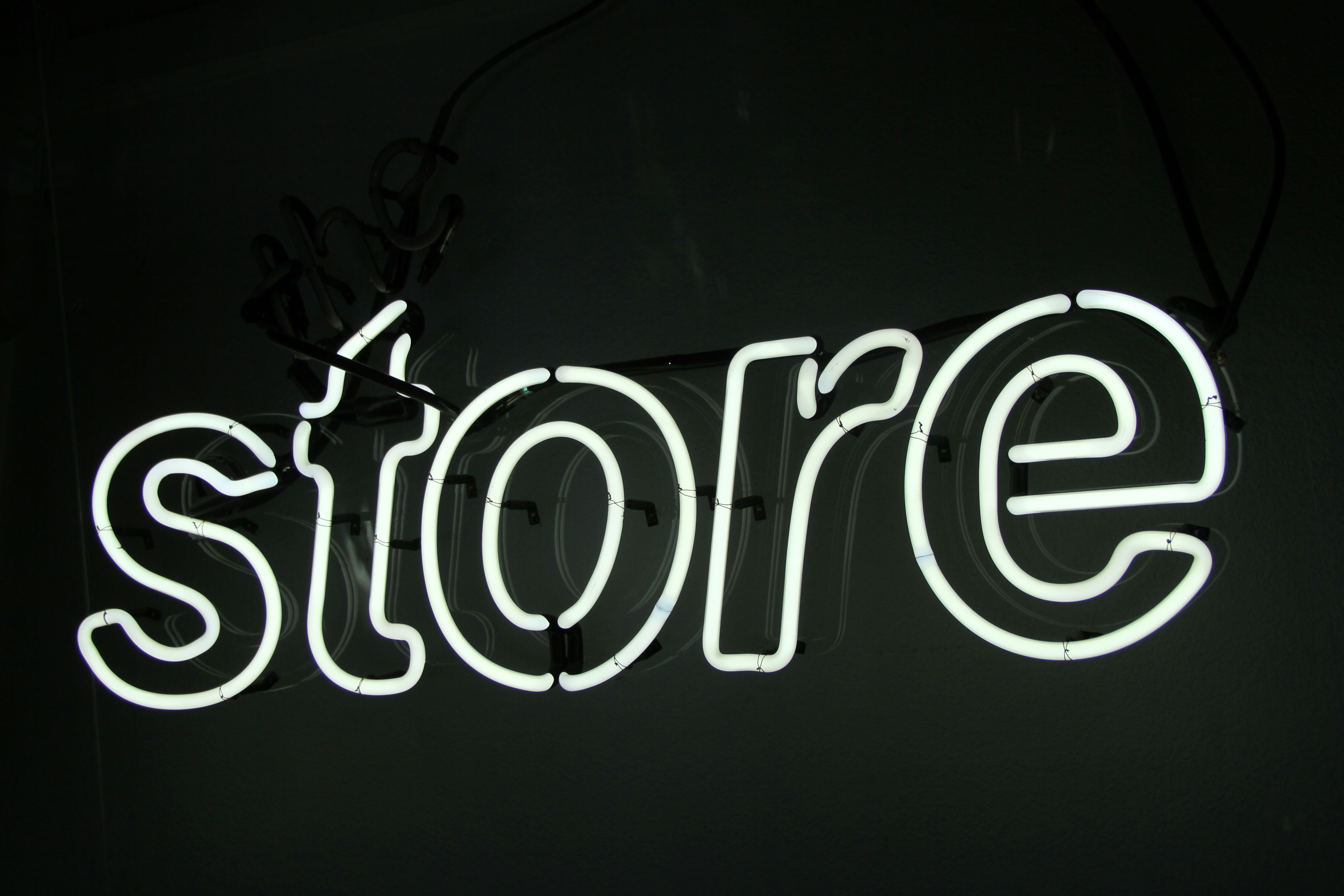 Biały neon z napisem „store” na ciemnej ścianie, grafika ogłoszenia statusu Shopify Premier Partner