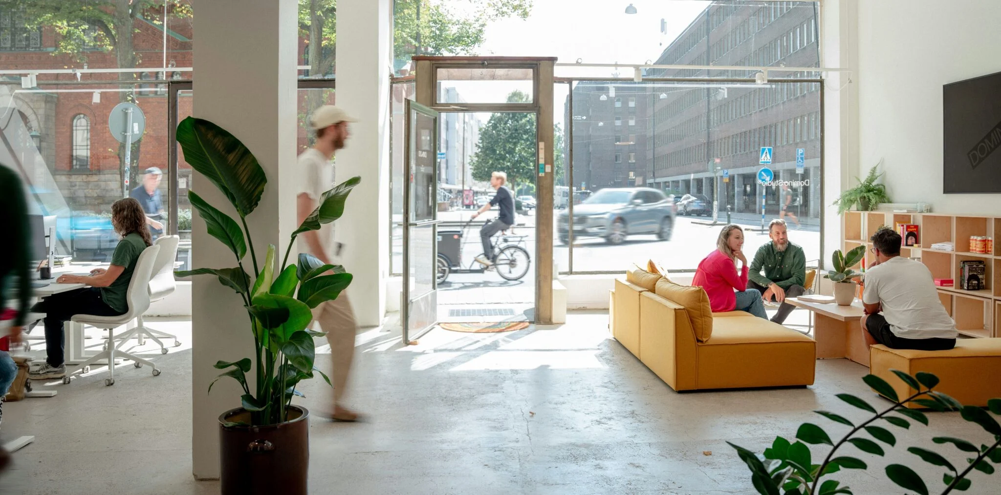 People working and chatting in a bright open-plan office with plants and a yellow sofa, a setting for customer journey mapping