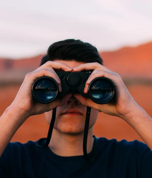 Young man looking through binoculars against a desert backdrop, symbolising a look at e-commerce trends