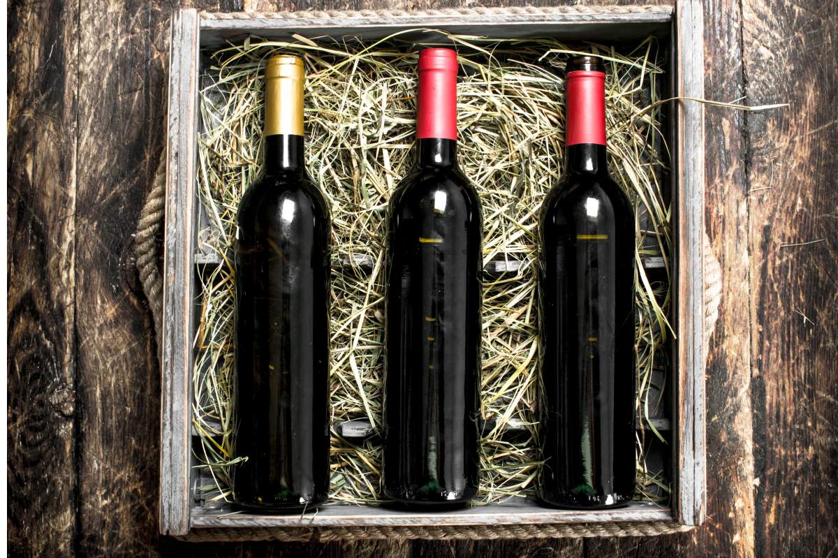 Three red wine bottles packed in straw inside a wooden crate, illustrating a subscription box delivery