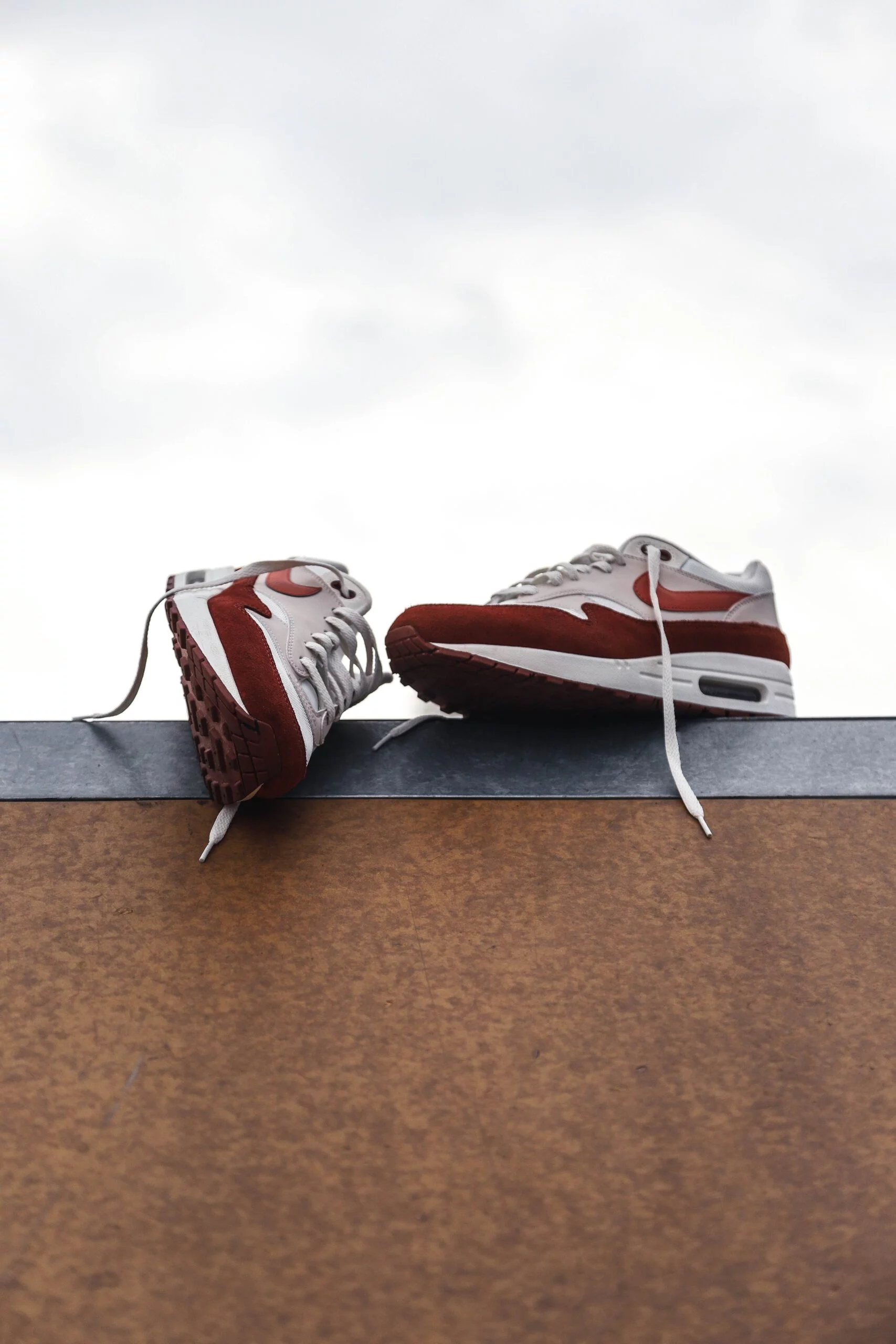 Pair of red and white Nike Air Max sneakers resting on a ledge against a cloudy sky, for selling footwear on Shopify