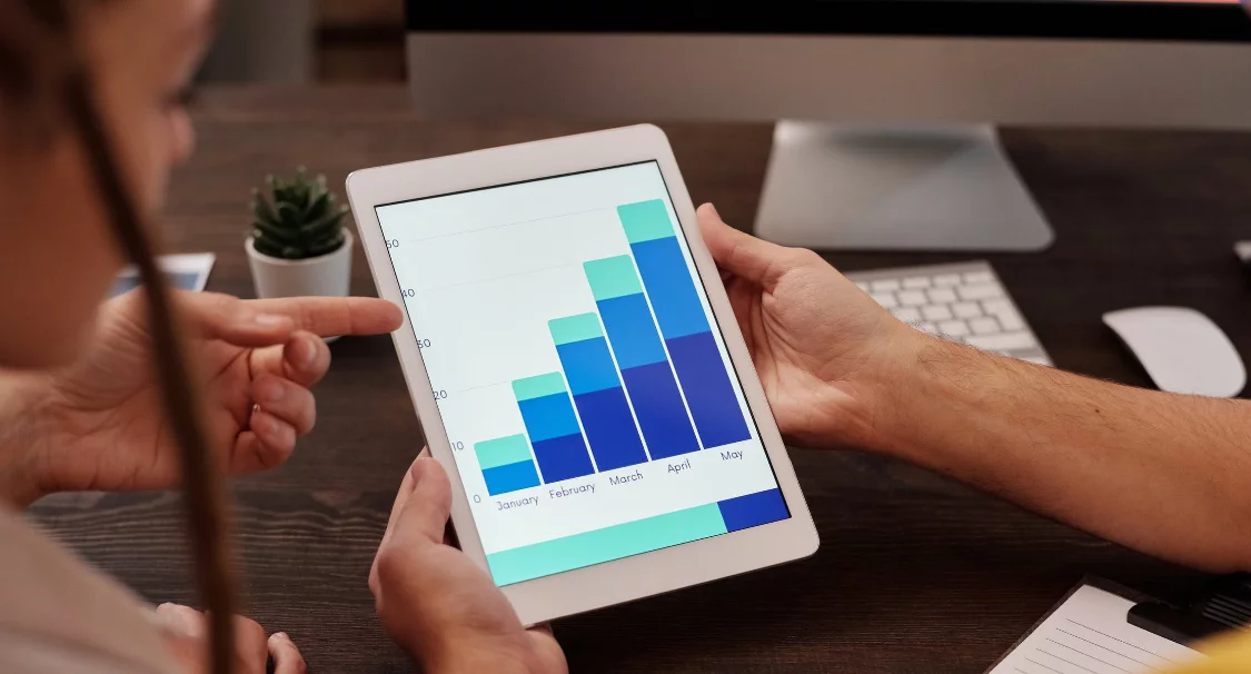 Two people reviewing a monthly bar chart on a tablet at a desk, illustrating Shopify analytics and reports
