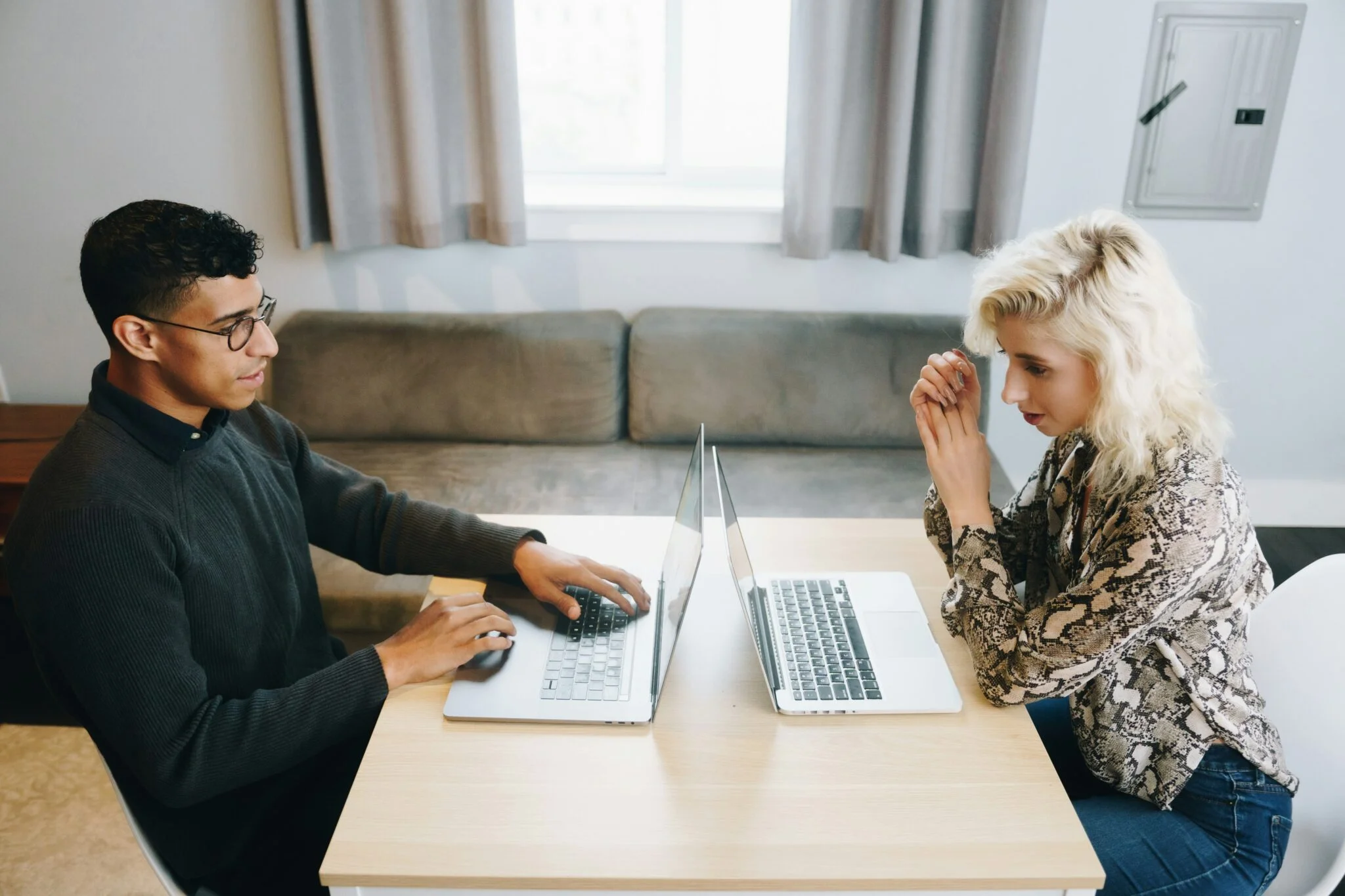 Man and woman sitting across a table with back-to-back laptops, symbolising the Magento vs. Shopify comparison