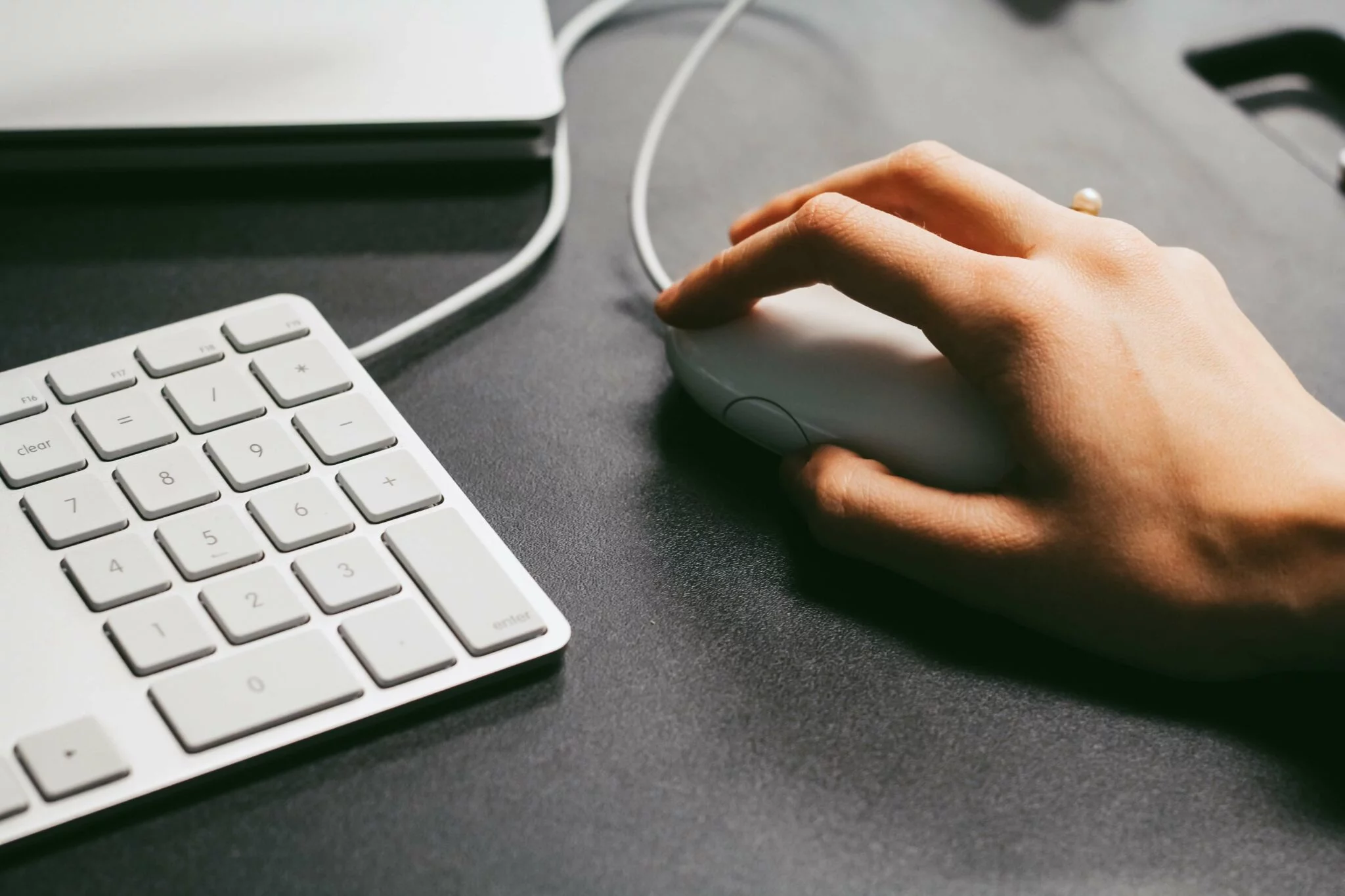 Hand on a white computer mouse next to a numeric keyboard on a dark desk, suggesting development work
