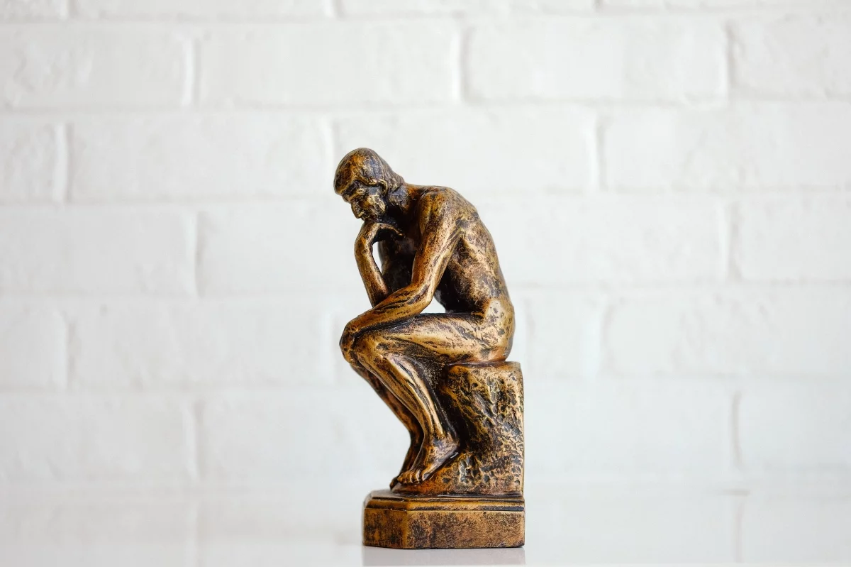 Bronze figurine of Rodin's 'The Thinker' against a white brick wall, representing questions from new Shopify store owners