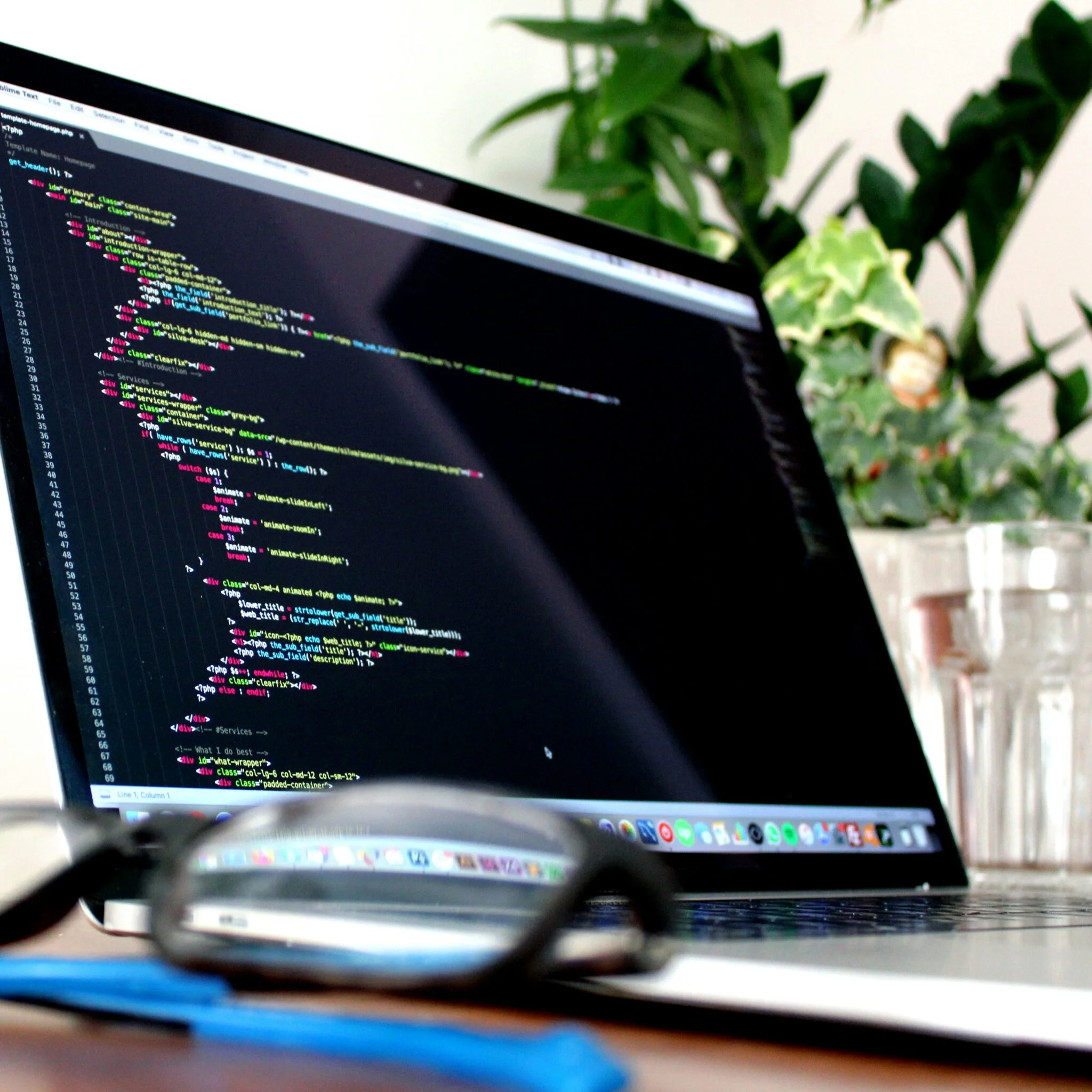 Laptop displaying lines of code beside plants, with glasses in the foreground, illustrating Shopify platform updates