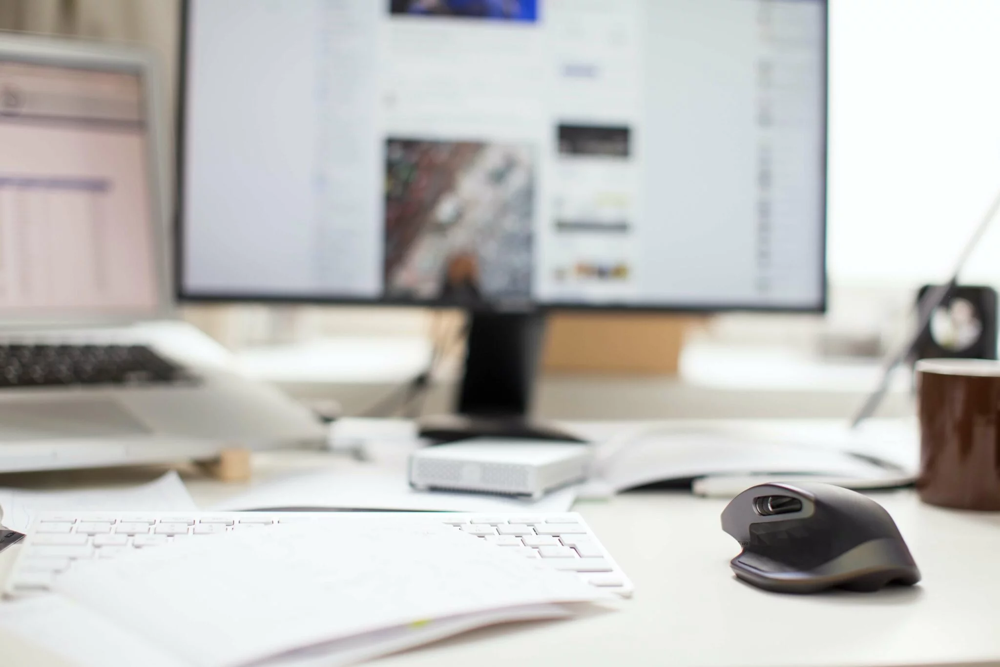 Blurred desk setup with a monitor, laptop, keyboard, mouse and mug, used for a Shopify POS guide