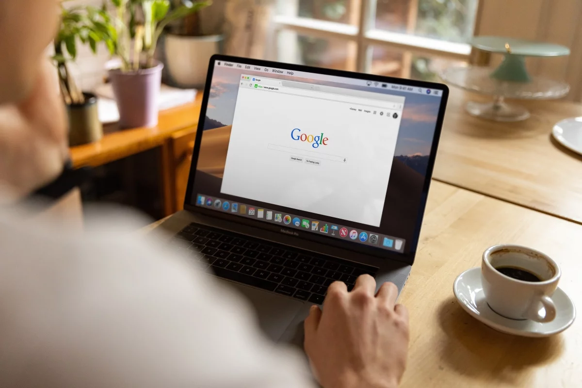 Person using a MacBook with the Google search page open, next to a cup of coffee, illustrating Shopify SEO