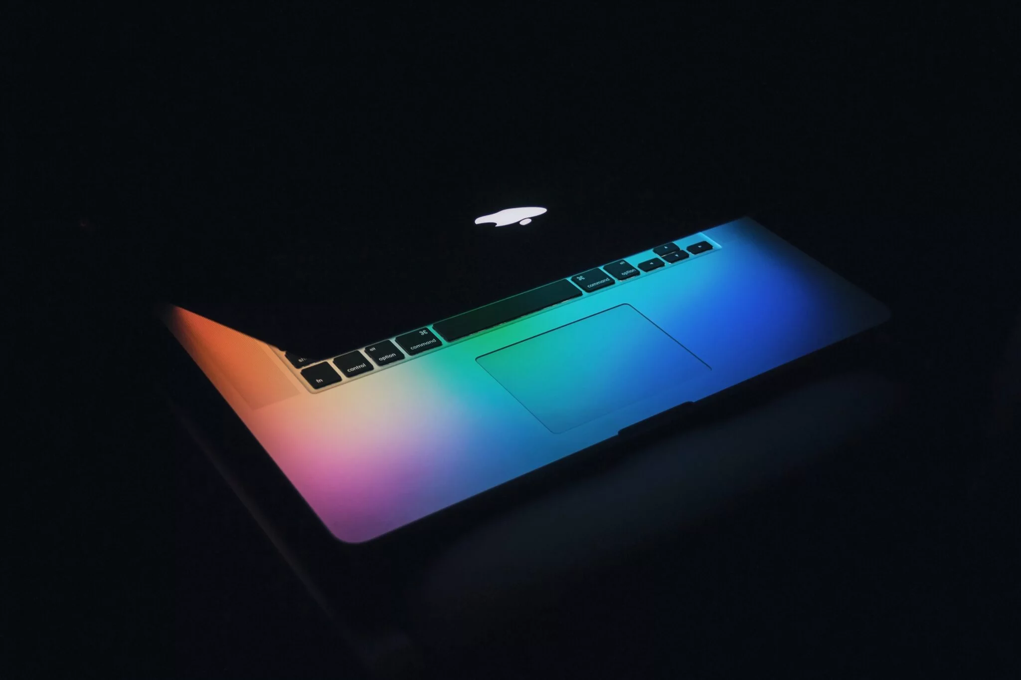 Half-open MacBook glowing with rainbow colours in a dark room, hinting at new Shopify features in 2023