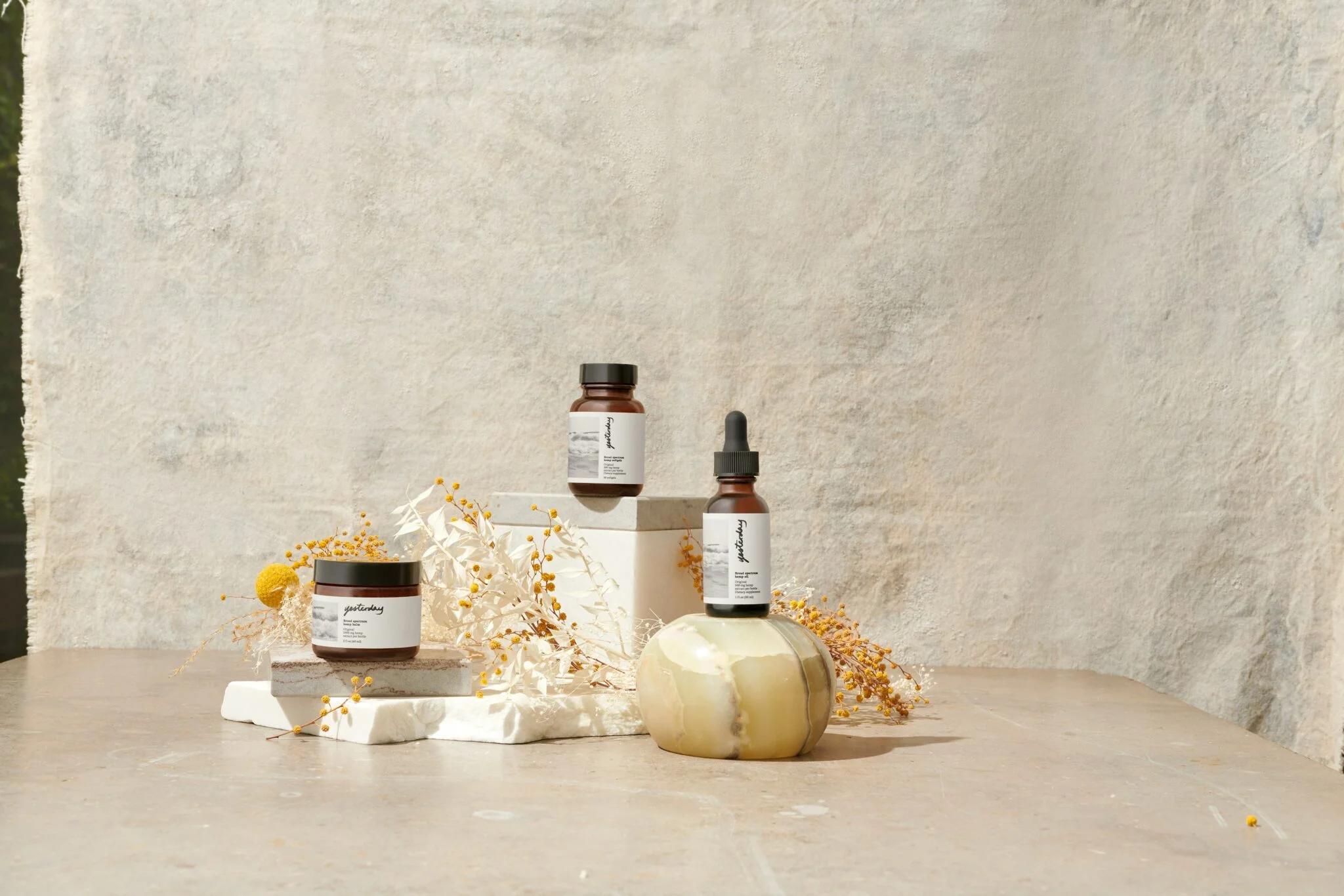 Amber skincare jars and a dropper bottle styled on stone blocks with dried yellow flowers, for a beauty store