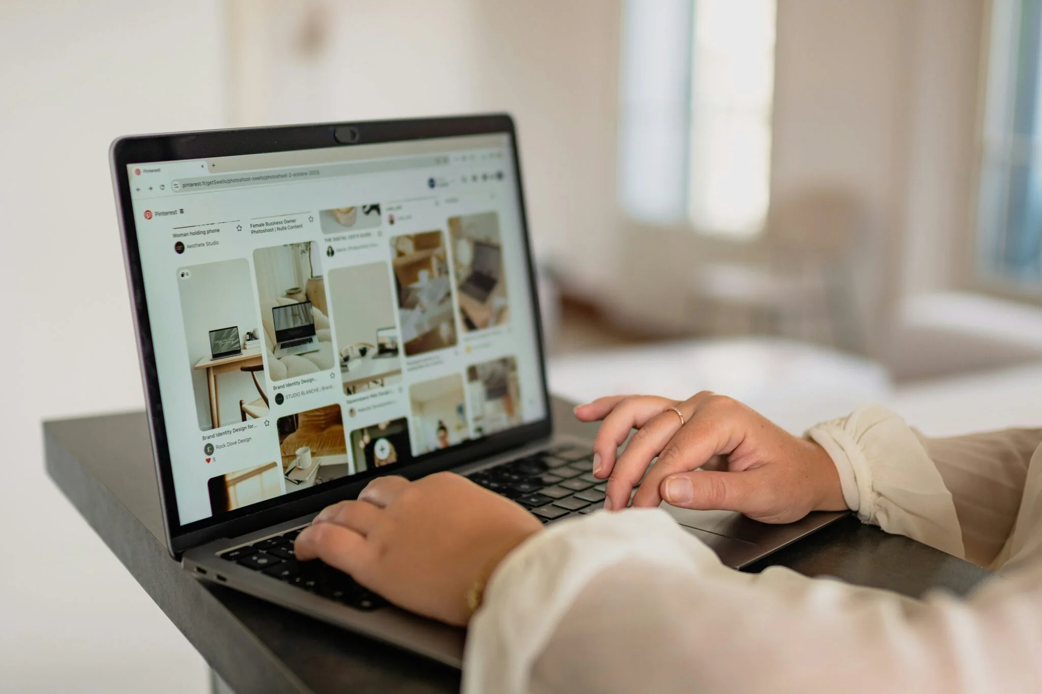 Hands typing on a laptop showing a Pinterest board with product ideas, researching trending products to sell on Shopify