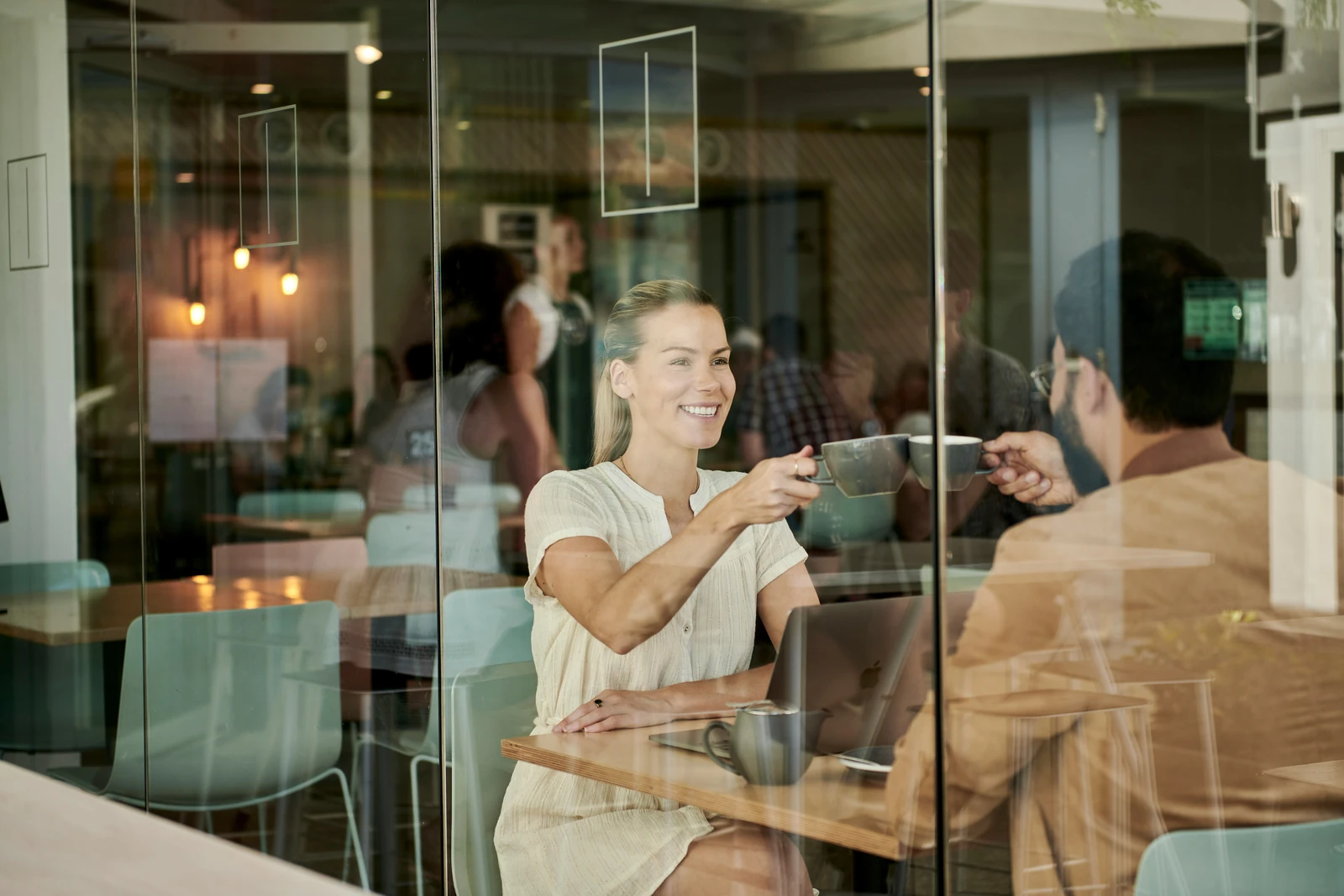 Woman and man toasting with coffee cups at a laptop in a glass-walled café, illustrating returning customers