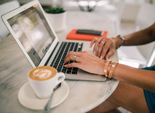 Kobieta pisze na laptopie przy marmurowym stoliku z cappuccino, symbolizując start własnego sklepu na Shopify