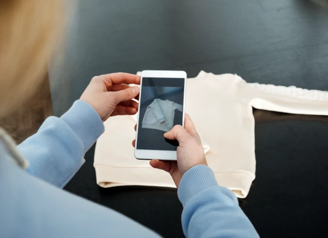 Kobieta fotografuje smartfonem kremową bluzę leżącą na stole, ilustrując nowe technologie w e-commerce fashion
