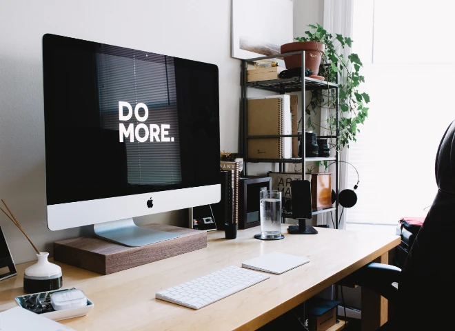 Biurko z iMakiem wyświetlającym napis „Do more.”, klawiaturą i regałem z roślinami, symbol automatyzacji pracy