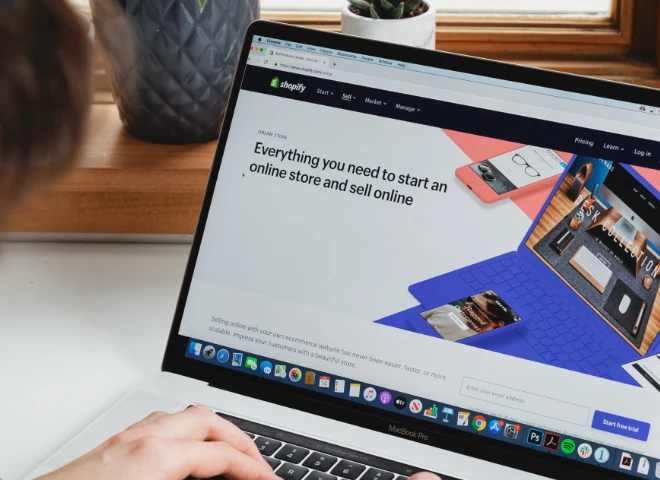 Osoba przegląda na MacBooku stronę Shopify z hasłem o wszystkim, czego potrzeba do założenia sklepu online