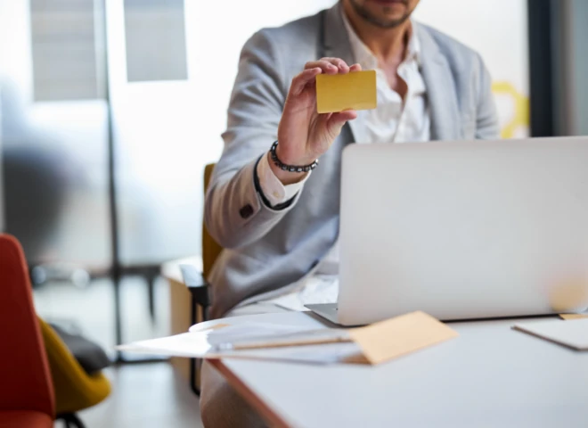 Mężczyzna w marynarce trzyma złotą kartę płatniczą przy laptopie, ilustrując płatności na Shopify