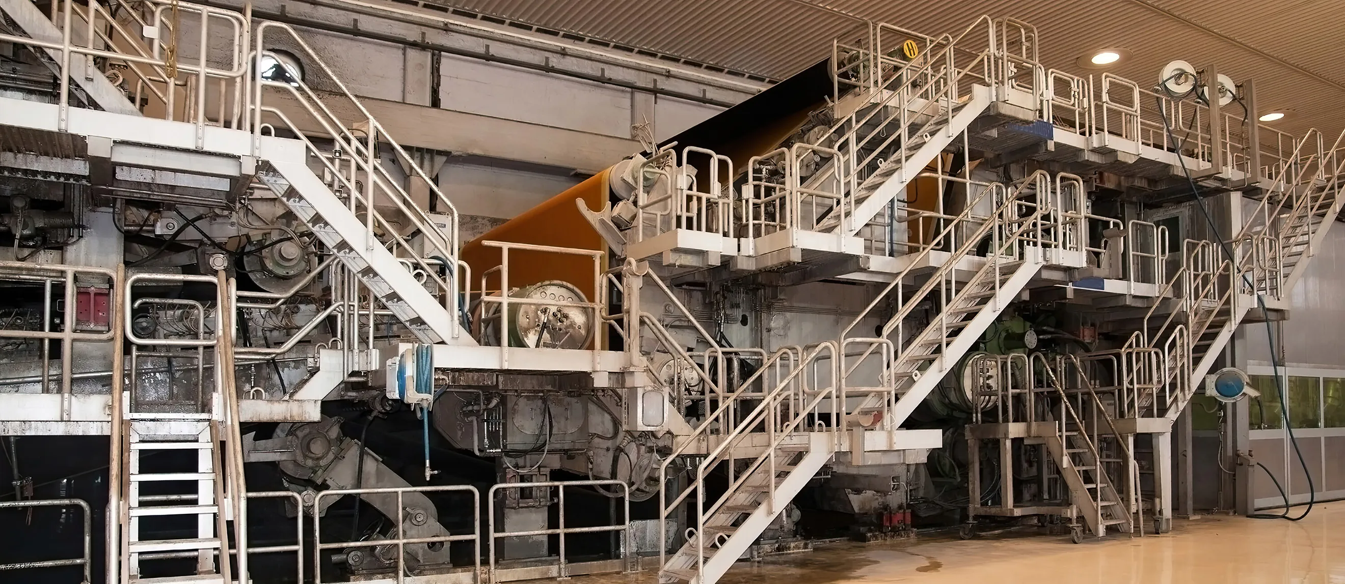 Industriemaschine mit mehreren weißen Metalltreppen und Geländern in einer Fabrikhalle.