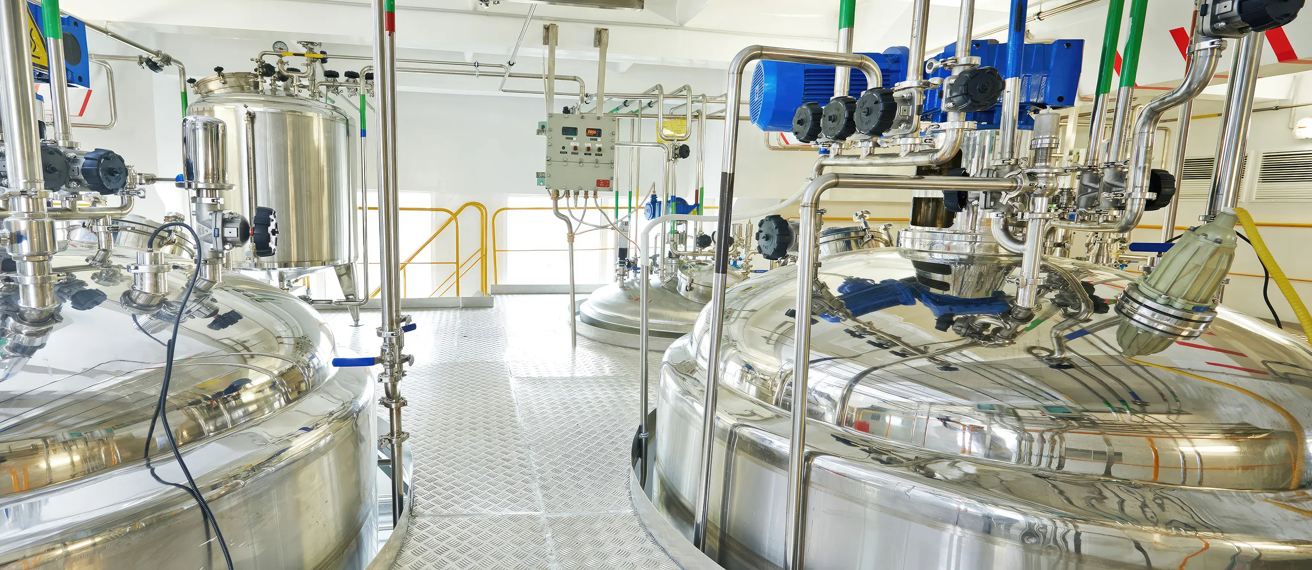Industrielle Anlage mit mehreren großen, silbernen Edelstahltanks und Rohrleitungen in einem hellen Raum.