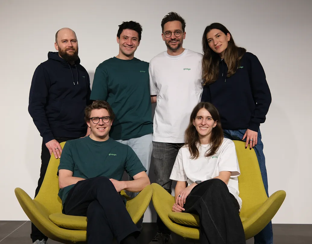 Sechs lächelnde Personen in Ginkgo-T-Shirts und Pullovern, zwei sitzen auf gelben Sesseln. ginkgo Team Bild.