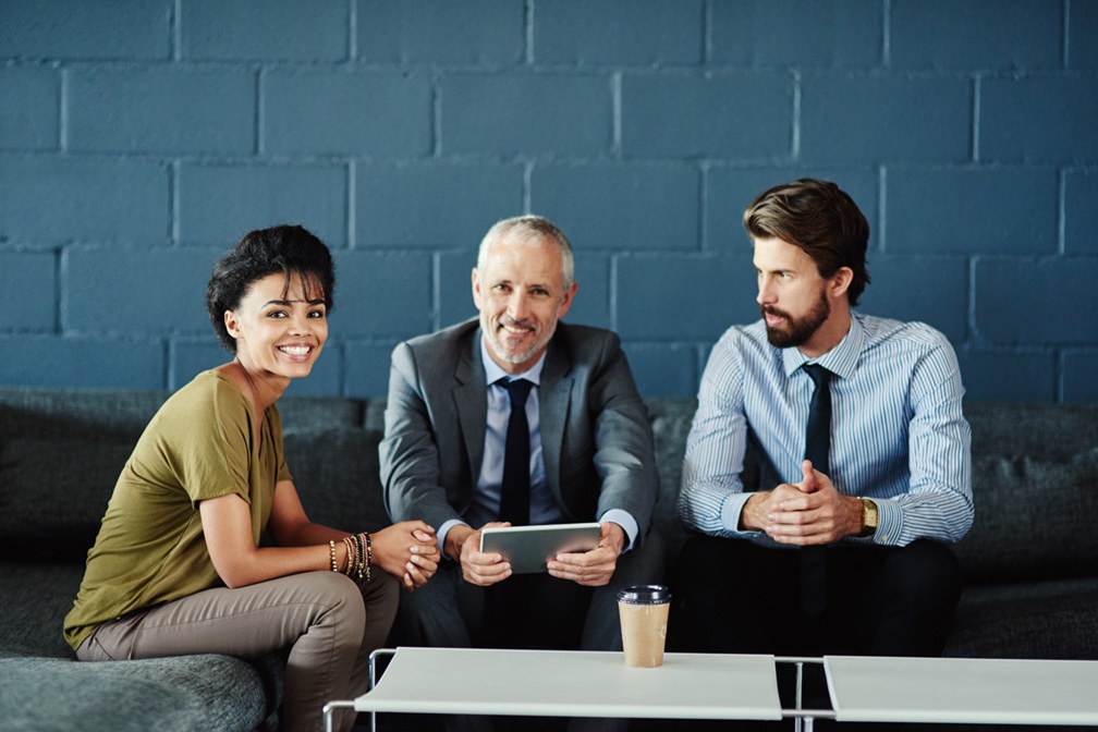Onboarding Support: Two colleagues sitting with a new hire, smiling, symbolising integration and support from day one.