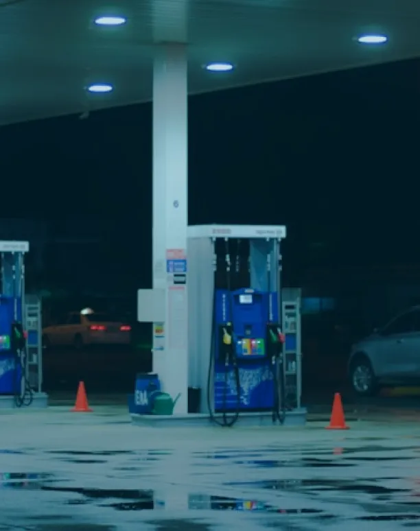 Gas pumps under canopy with wet ground.