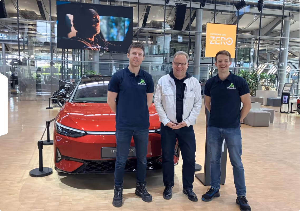 Three men standing in front of a red Volkswagen ID.3 X electric car inside a modern showroom with glass walls and an 'Experience Our Zero' sign.