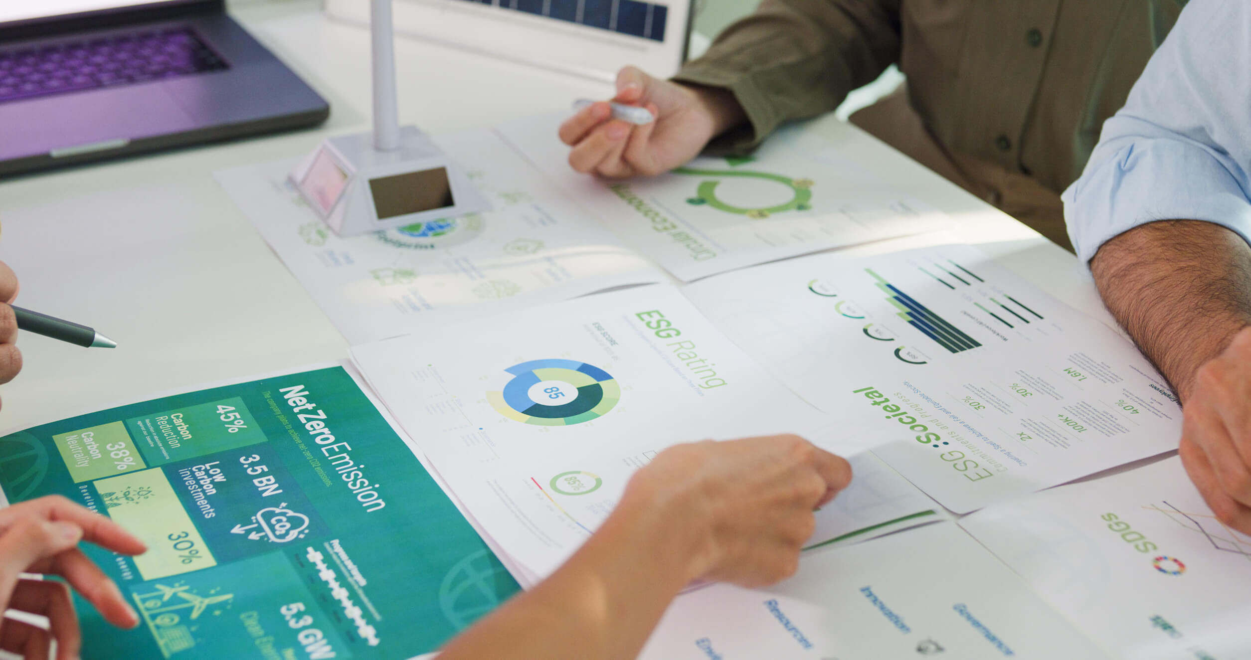 People reviewing ESG rating, Net Zero Emission, and sustainability reports on a table next to a laptop.