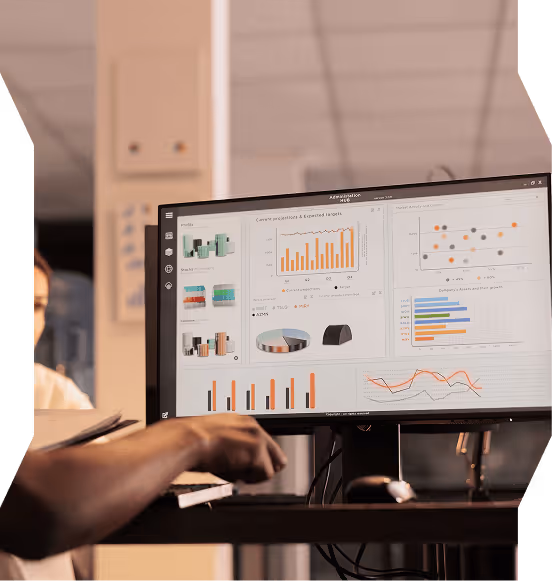 Person working at a desk with a monitor displaying multiple colorful charts and graphs related to data analytics.