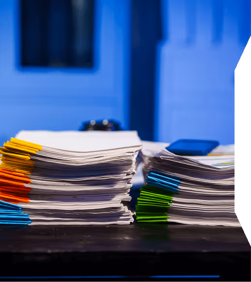 Stacks of documents organized with colorful paper clips in yellow, orange, blue, green, and teal on a dark table.