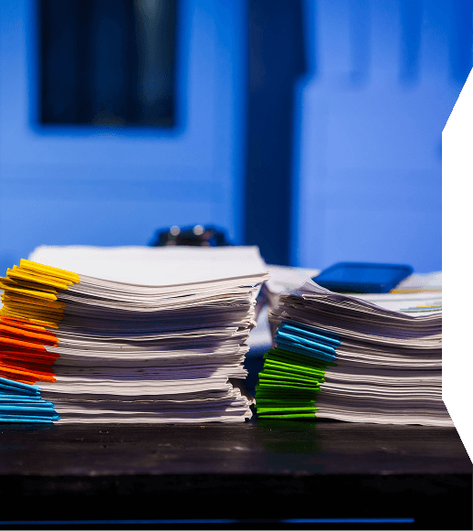 Stacks of documents organized with colorful paper clips in yellow, orange, blue, green, and teal on a dark table.