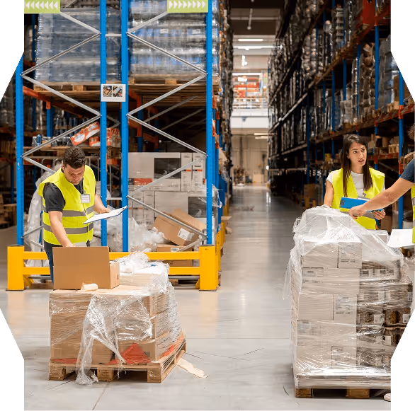 Warehouse workers in yellow safety vests inspecting and organizing pallets of boxes wrapped in plastic.