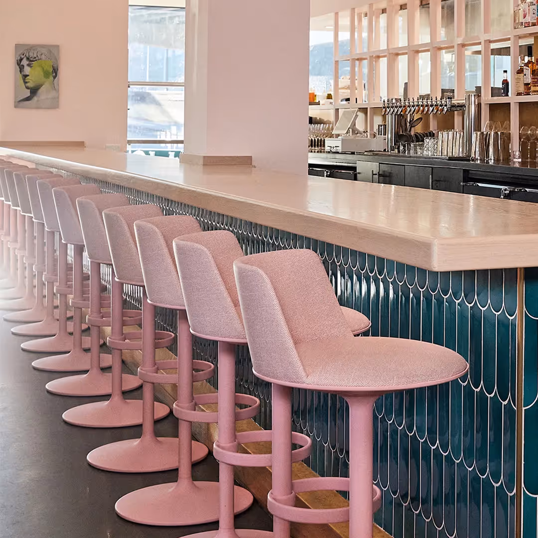 Contemporary bar interior with pink pedestal stools, scalloped teal tile front, and stylised portrait artwork