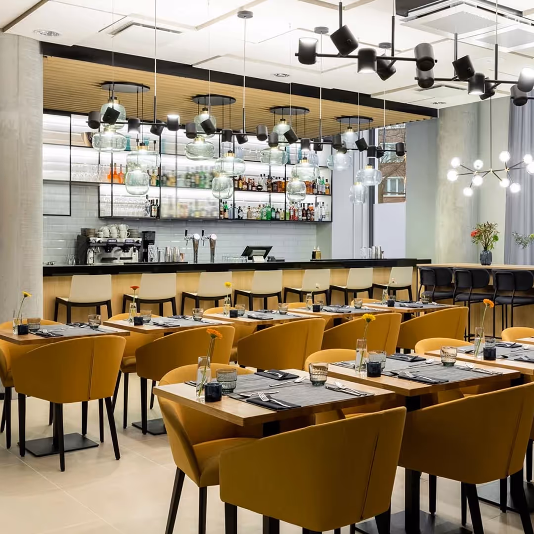 Marriott Courtyard restaurant with mustard-yellow chairs, wooden tables, and well-lit bar backdrop featuring glass light fixture