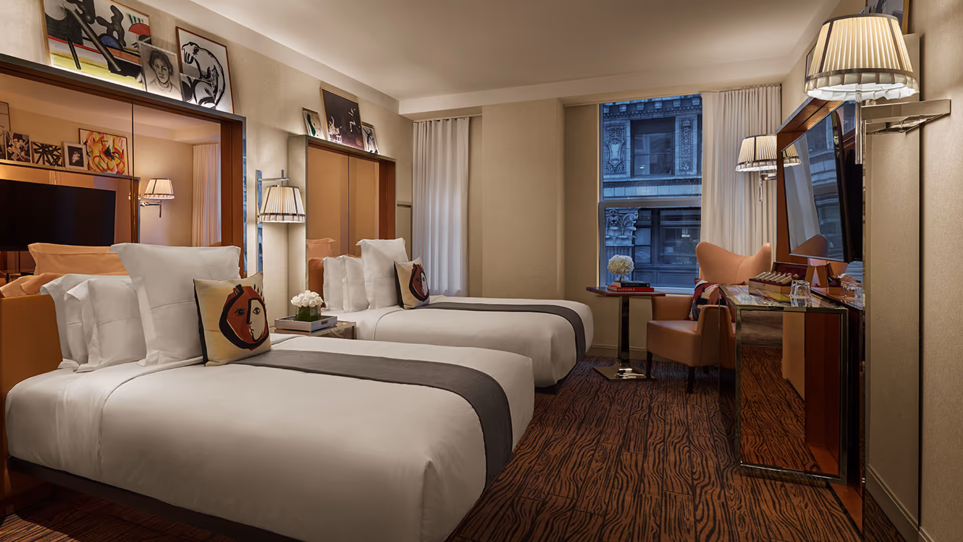 Mondrian hotel room with 1902 case goods, twin beds, artistic pillows, wall-mounted lamps, and gallery-style framed artwork above headboards