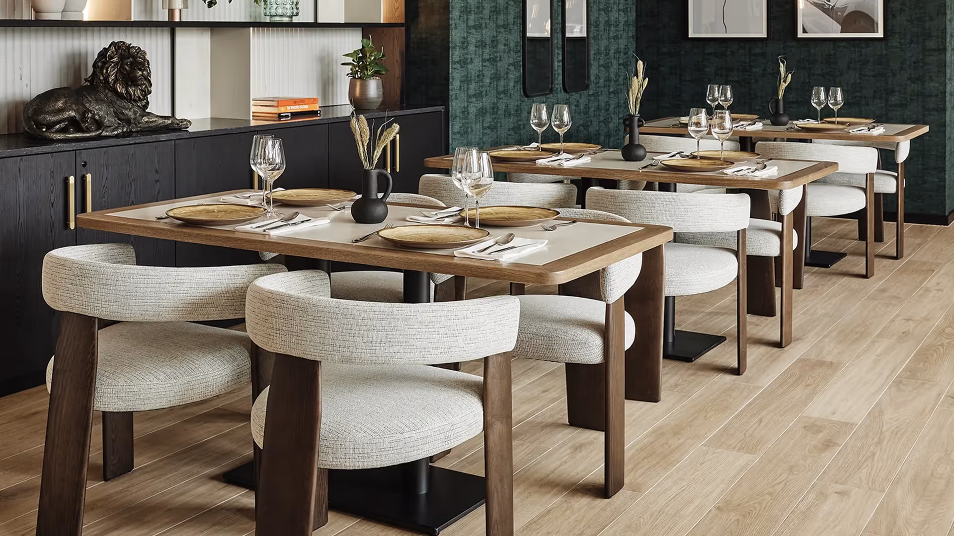 Elegant dining space with 1902 Oru chairs, golden plates, and a green textured wall featuring framed artwork and a lion sculpture