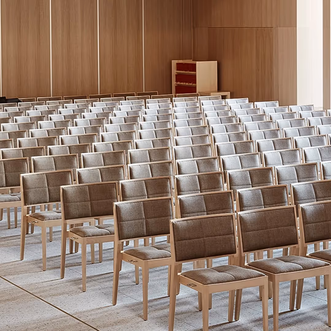 Modern church hall with rows of cushioned 1902 Manila chairs on neutral flooring, facing forward in grid layout beneath light wood panelled walls