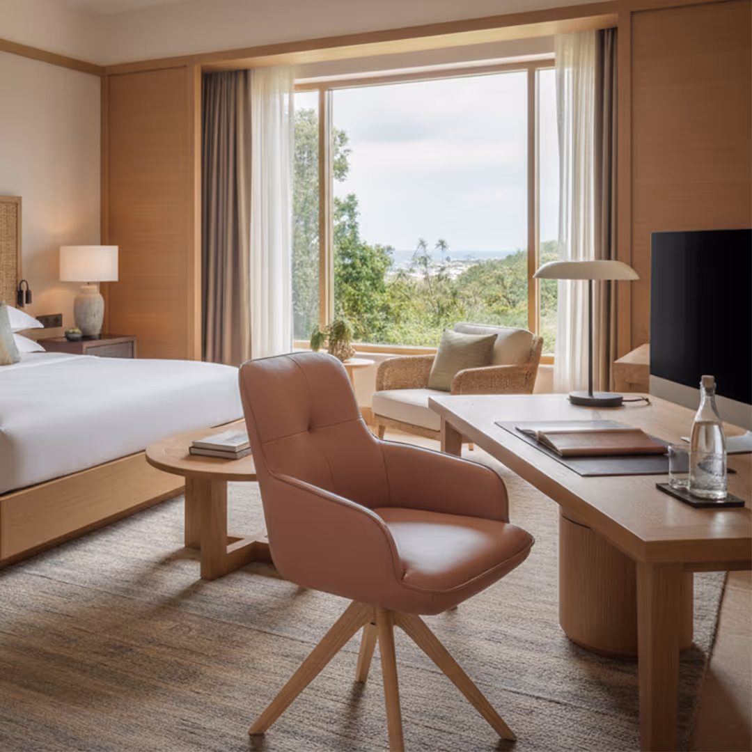 Resort hotel bedroom with wood desk, 1902 Bora swivel chair, white linens, and scenic view through large window