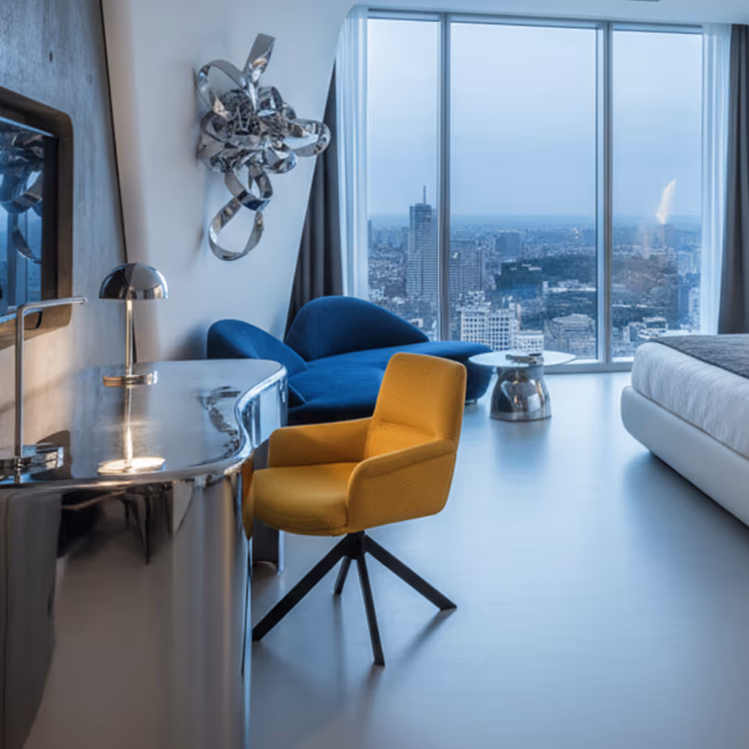 Modern hotel room with chrome desk, 1902 Leste yellow swivel chair, blue lounge chair, and panoramic city view