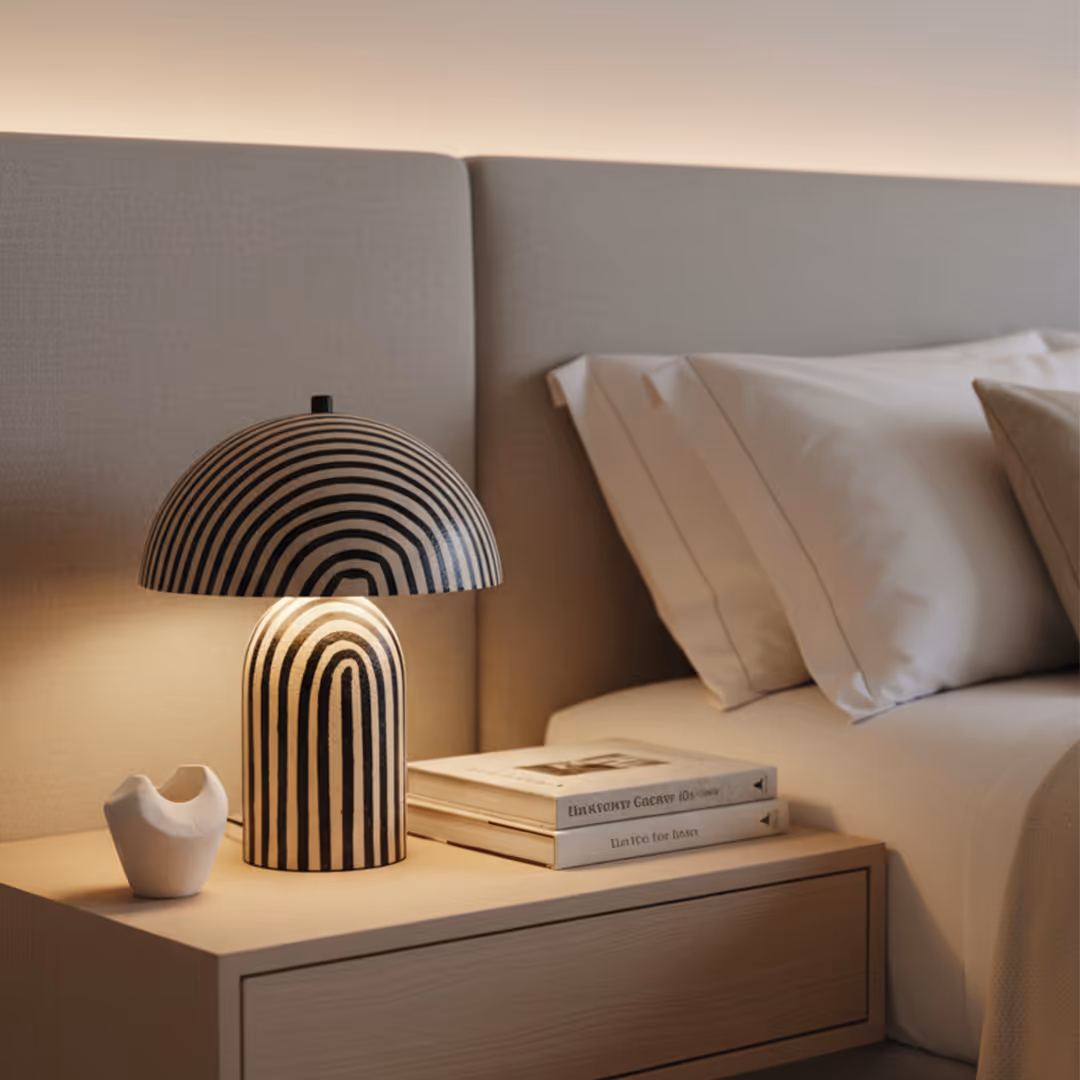 Minimalist bedroom with 1902 Marlborough striped dome lamp, abstract sculpture, stacked books, and beige upholstered headboard