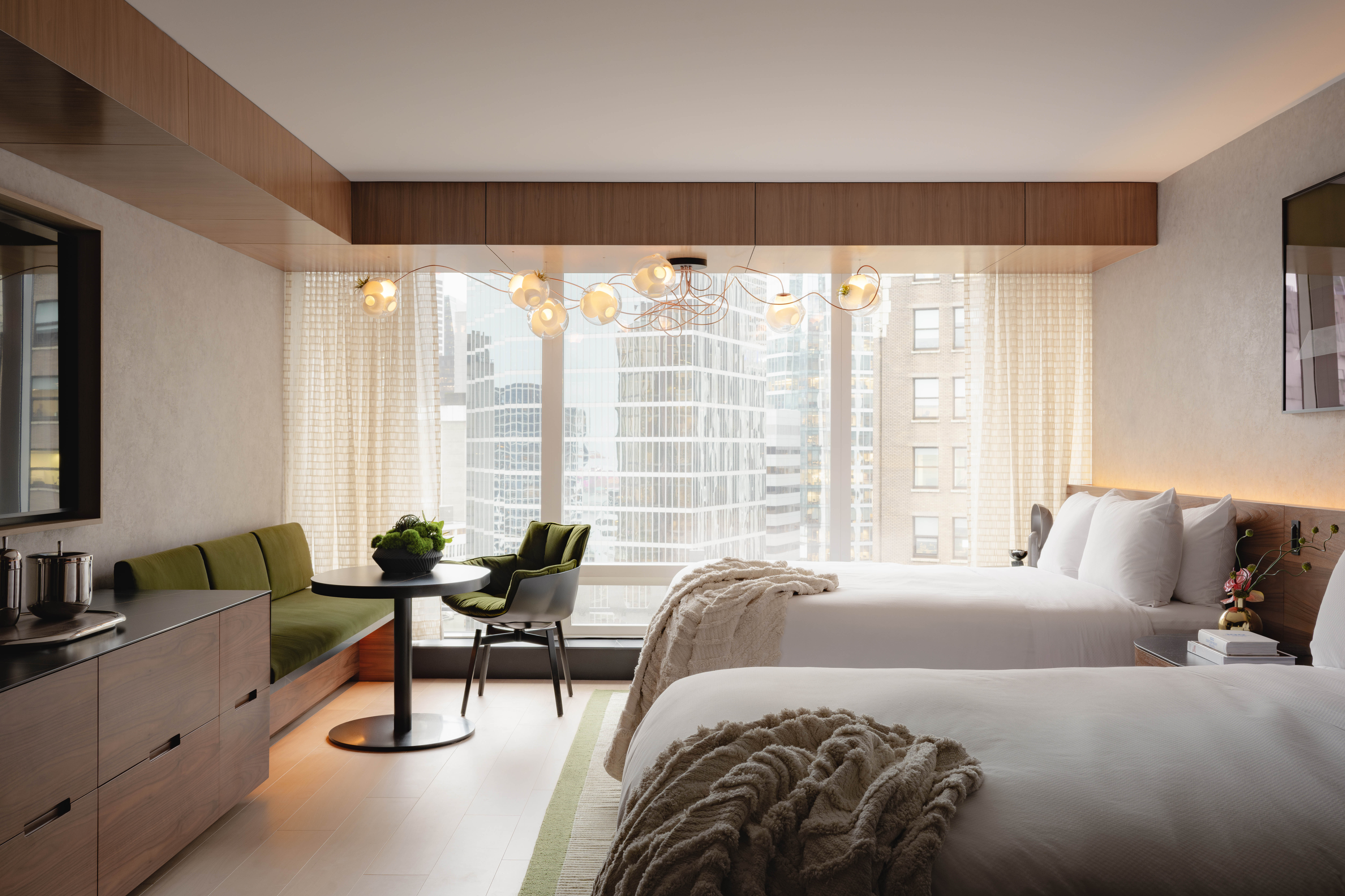 Elegant guestroom at Fairmont Pacific Rim with plush twin beds, city views, and a cozy green seating nook.