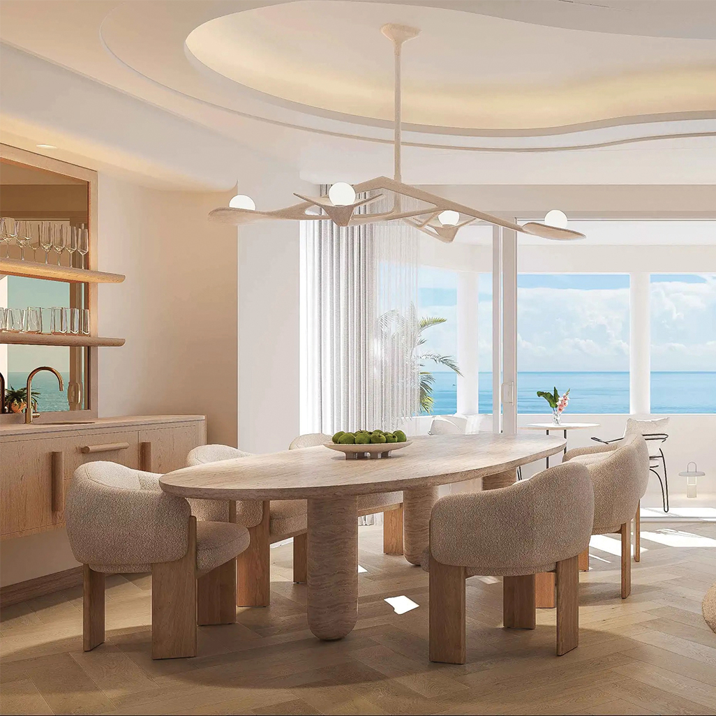 Serene coastal dining space with beautifully curved upholstered chairs, a sculpted wood table, and ocean views beyond soft drapery.